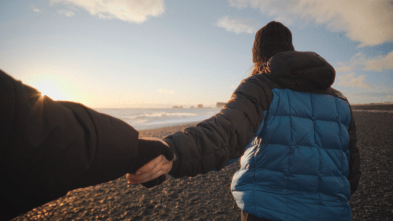 Man en vrouw houden handen vast op black sand beach IJsland